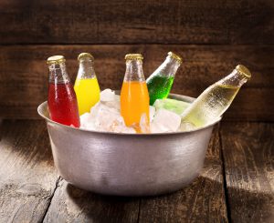 various bottles of soda in the bucket with ice on wooden table