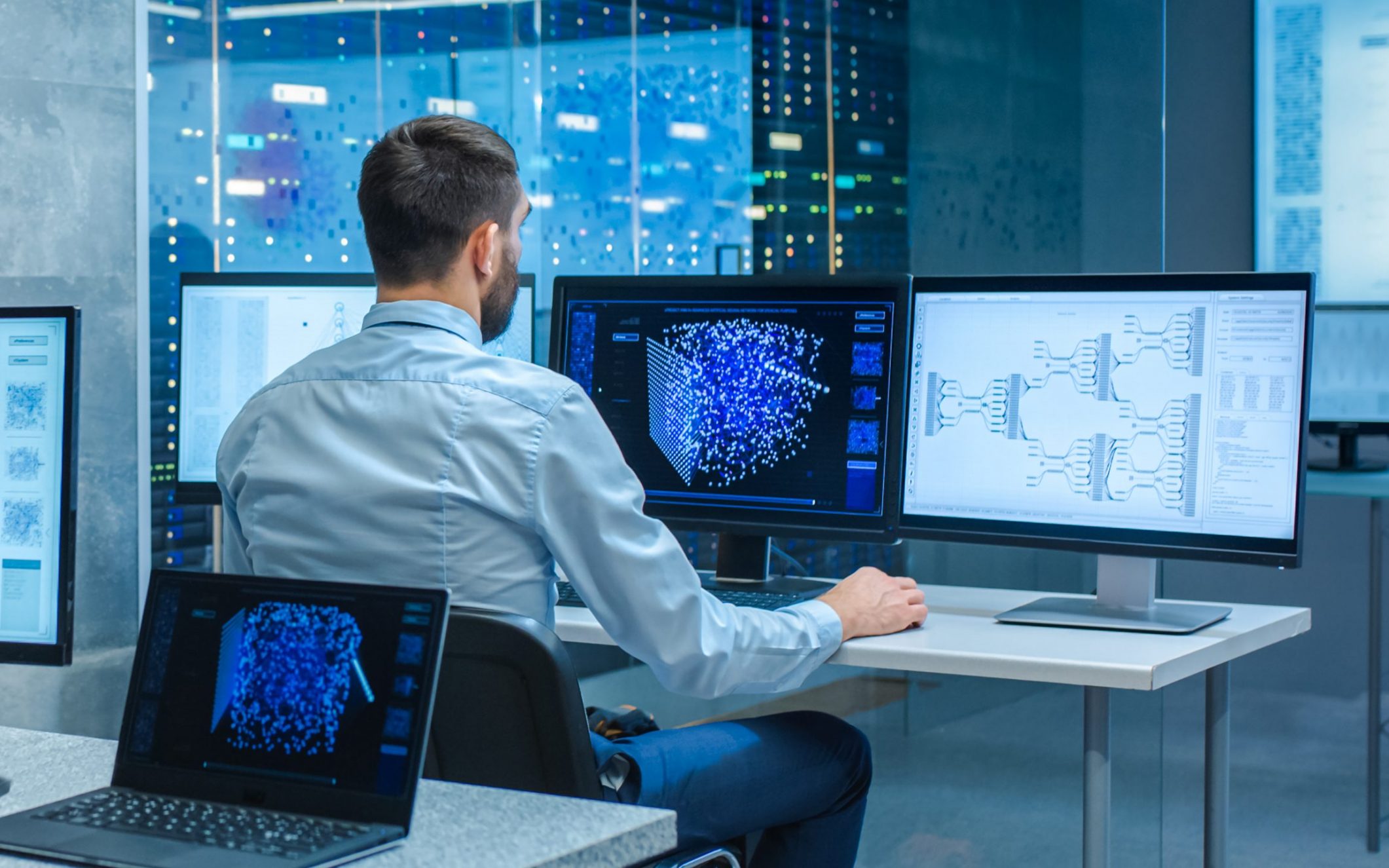 Beautiful Male Computer Engineer and Scientists Create Neural Network at His Workstation. Office is Full of Displays Showing 3D Representations of Neural Networks.